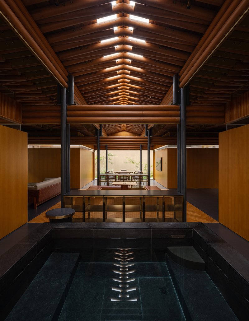 Indoor bath with dark tile surround beneath a vaulted timber ceiling with steel bracing