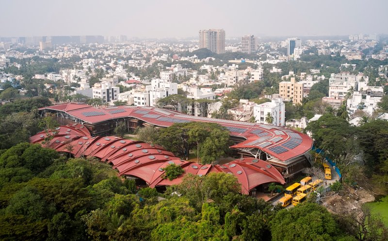Aerial view of the undulating terracotta metal roof with solar panels overlooking a dense urban neighborhood