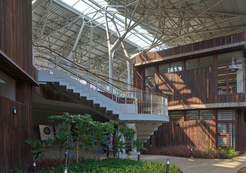 Planted courtyard with a curving staircase connecting levels under dappled sunlight through the space frame