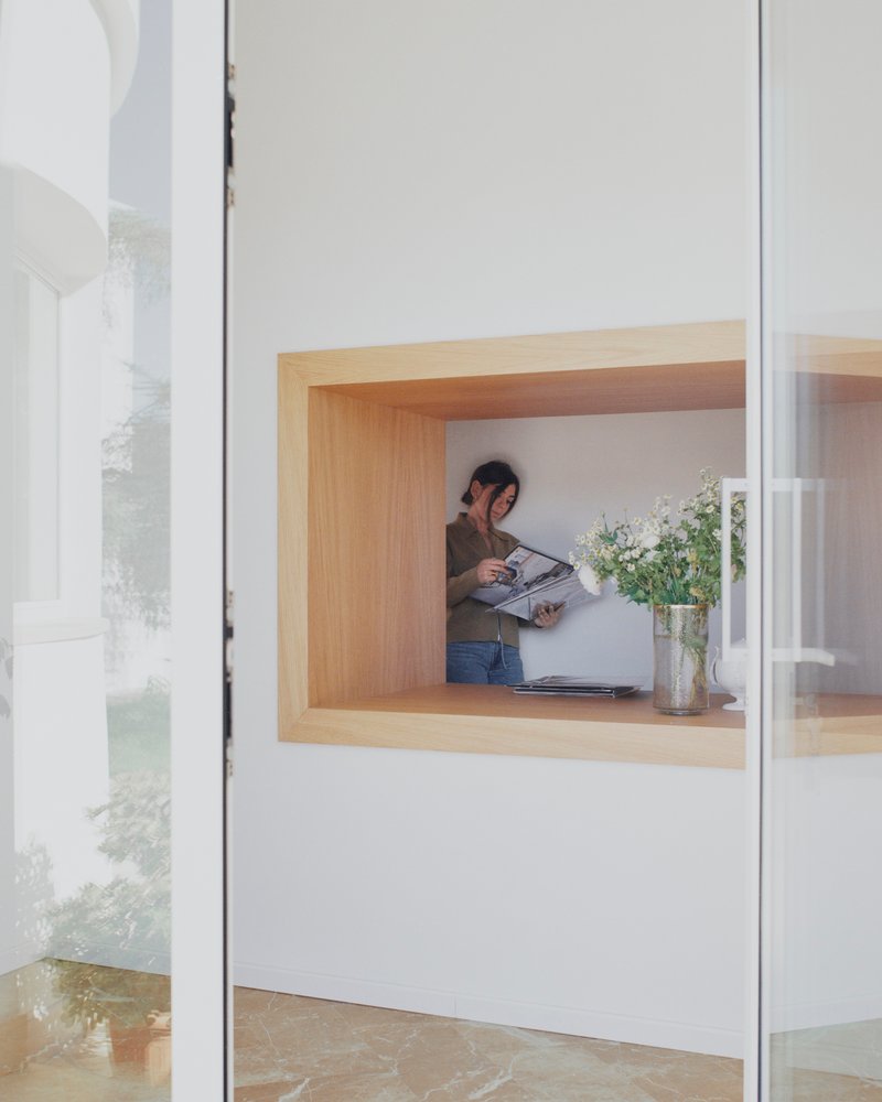 Timber-lined window nook with a person reading while standing beside a vase of flowers