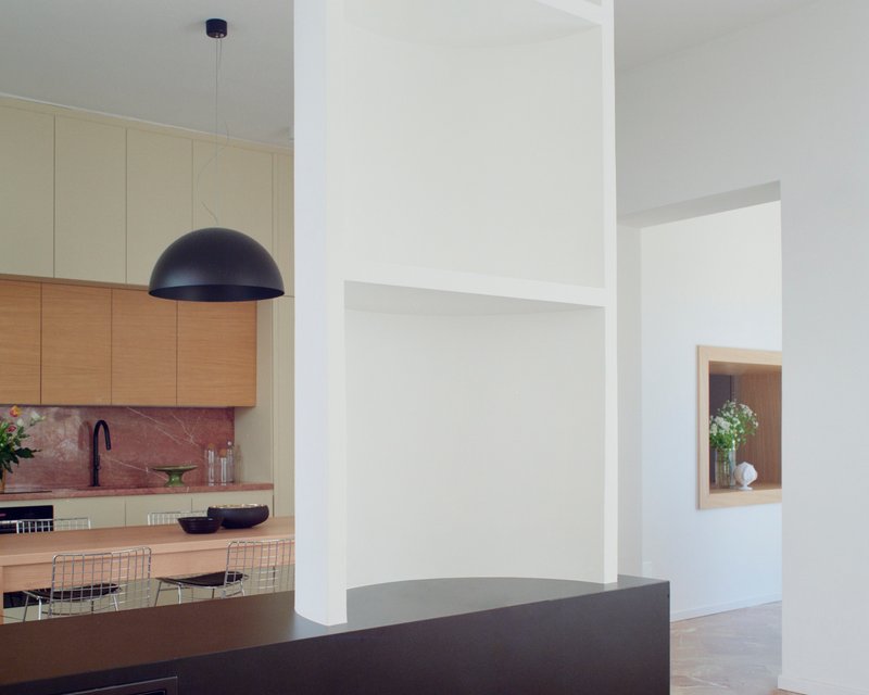 Open plan interior with kitchen visible beyond a dark island and recessed wall niche framing vases