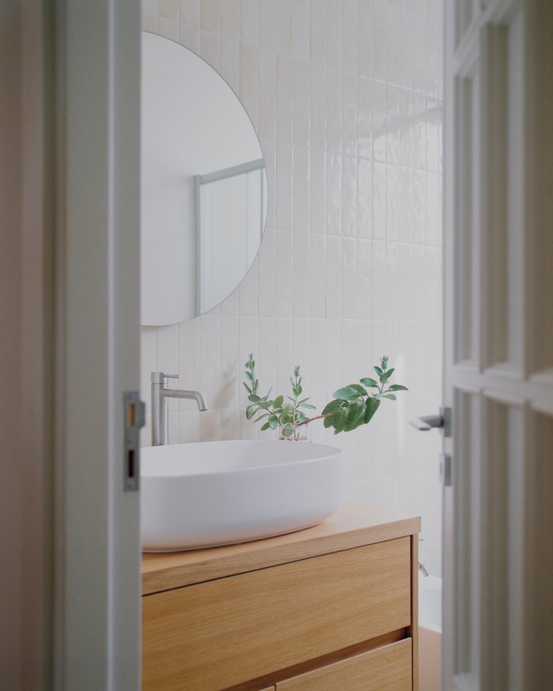 Bathroom vanity with vessel sink on oak cabinetry beneath vertical white tiles and a round mirror