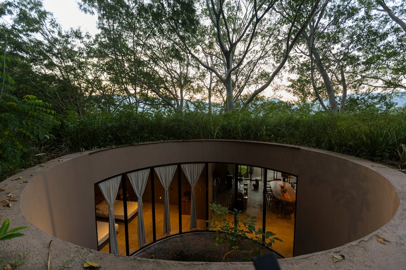Circular courtyard with glazed doors opening to the interior beneath a grass-covered roof edge at twilight