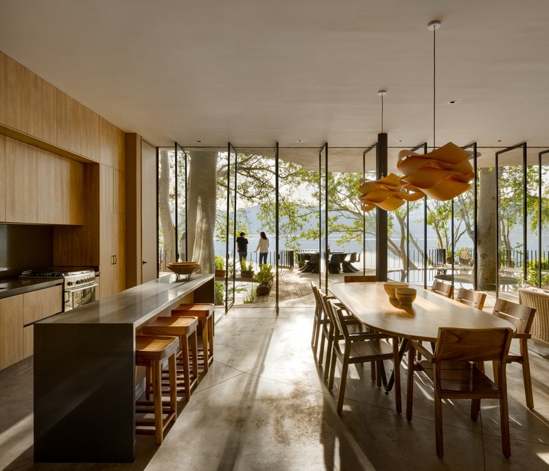 Kitchen and dining area with island, timber cabinetry, and floor-to-ceiling glass opening to the terrace