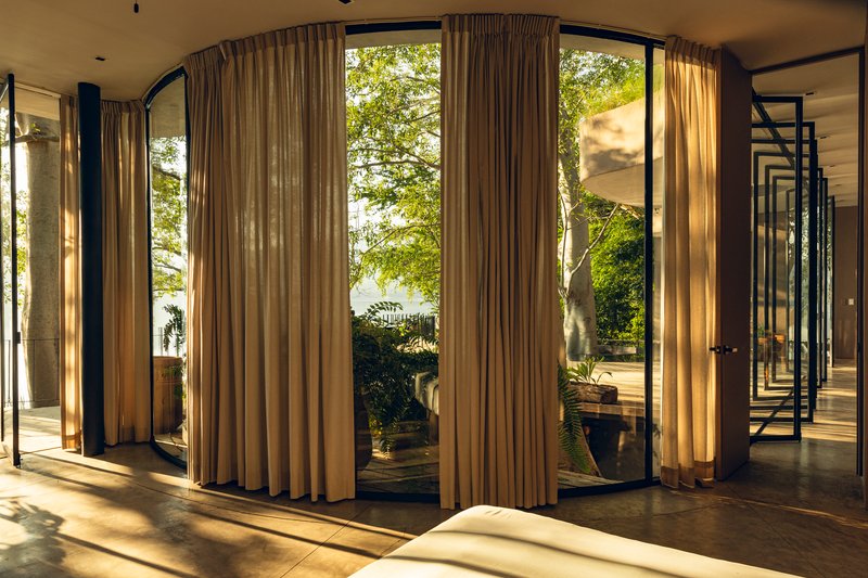 Floor-to-ceiling curtains framing glazed doors that open to a planted terrace in afternoon light