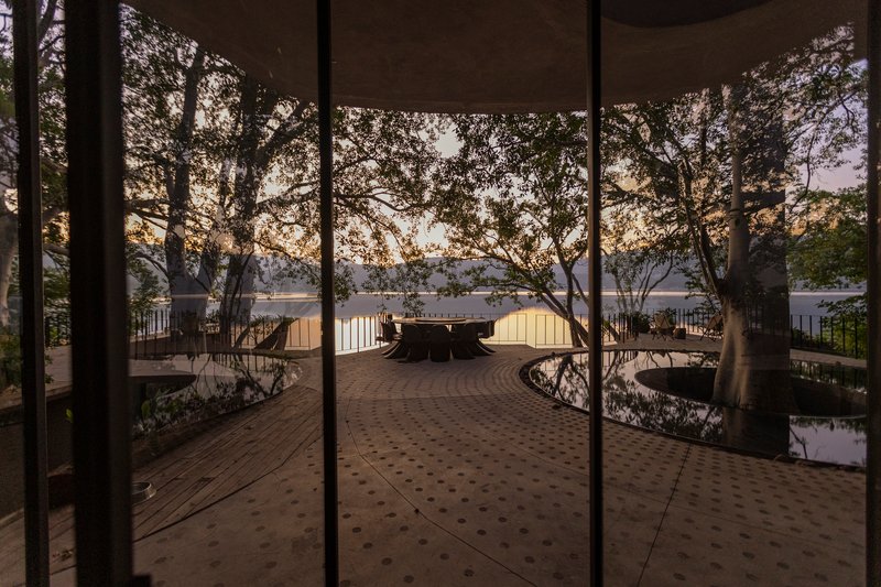 View through glass doors to an elevated timber deck with preserved trees and a distant lake at dusk