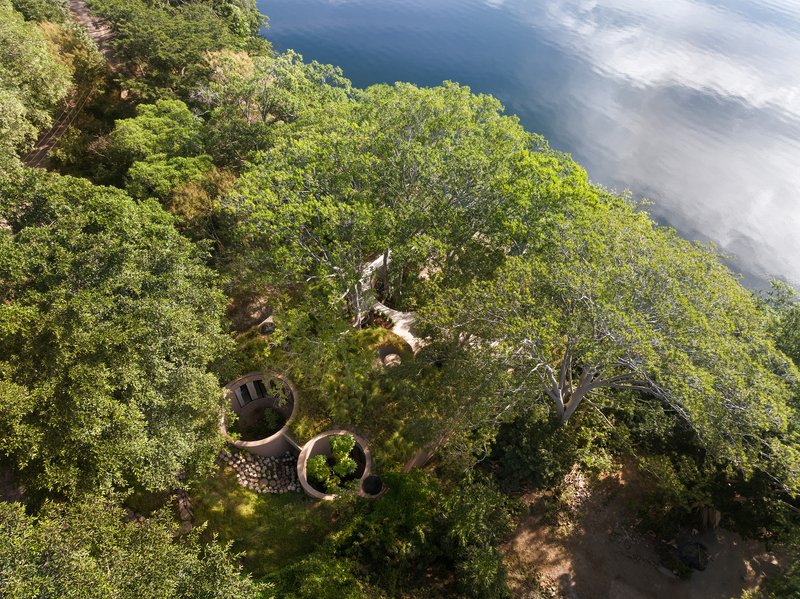 Aerial view of the curved roof structures nestled among dense tree canopy and open waterfront