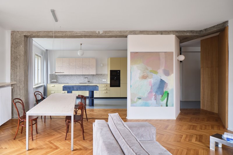 Open-plan living space with exposed concrete beams, herringbone oak floor and freestanding white partition with artwork