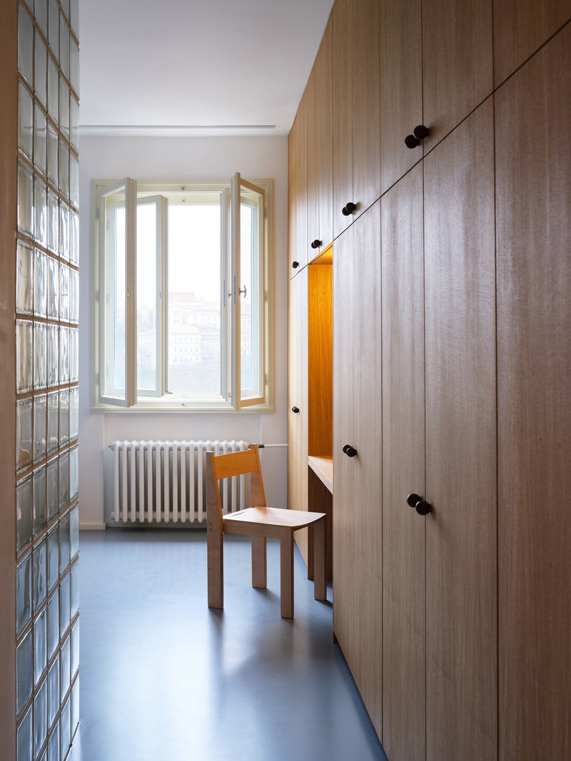 Narrow room with glass block wall, timber wardrobe and open window above a white radiator
