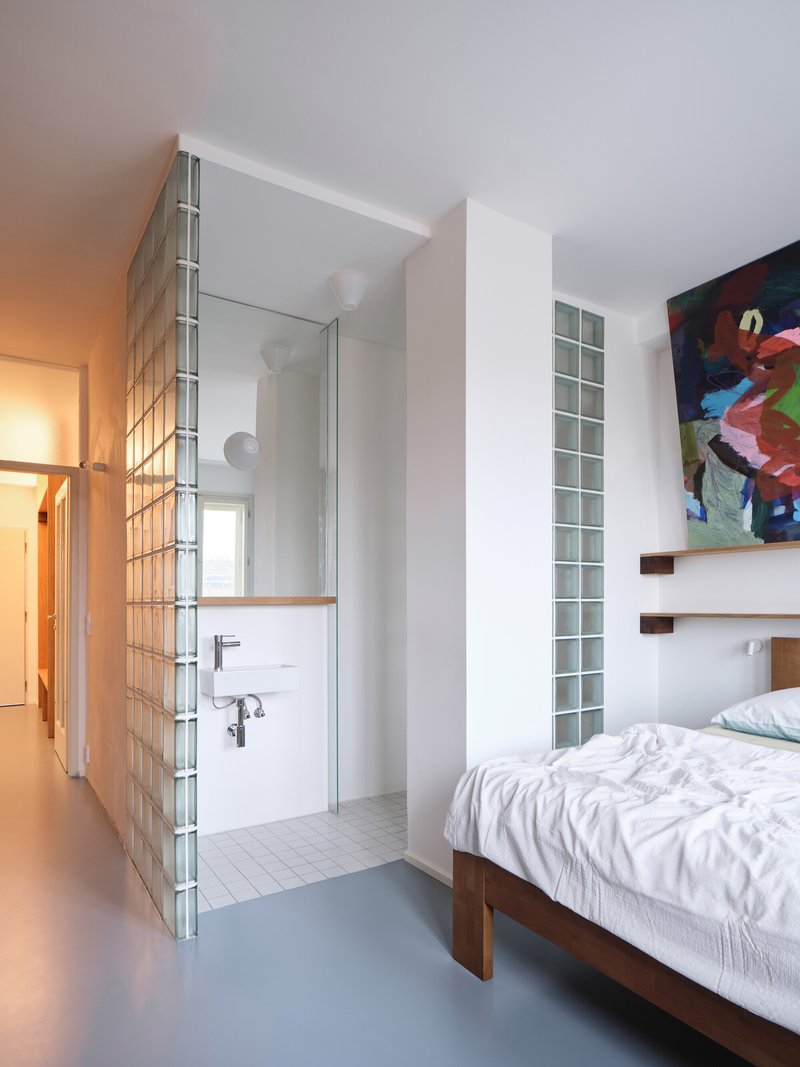 Bedroom corner showing glass block partition screening a bathroom with twin sinks and warm ceiling light