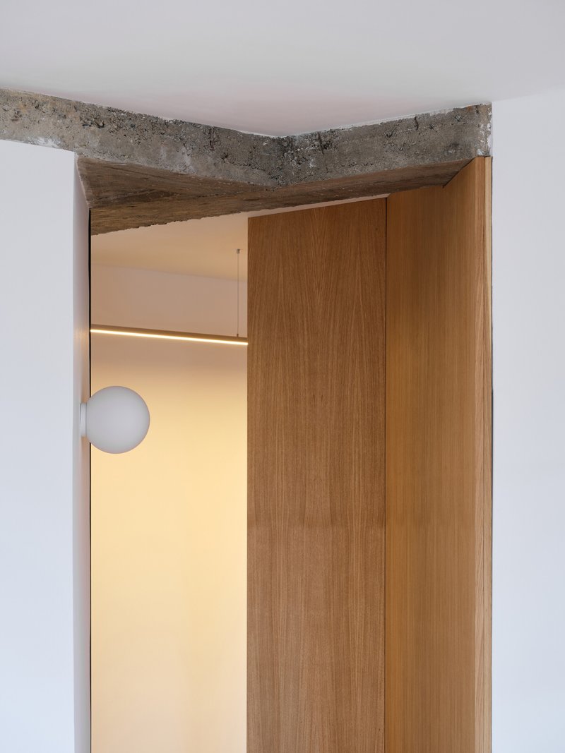 Doorway detail showing exposed concrete lintel above timber door frame with globe light visible beyond