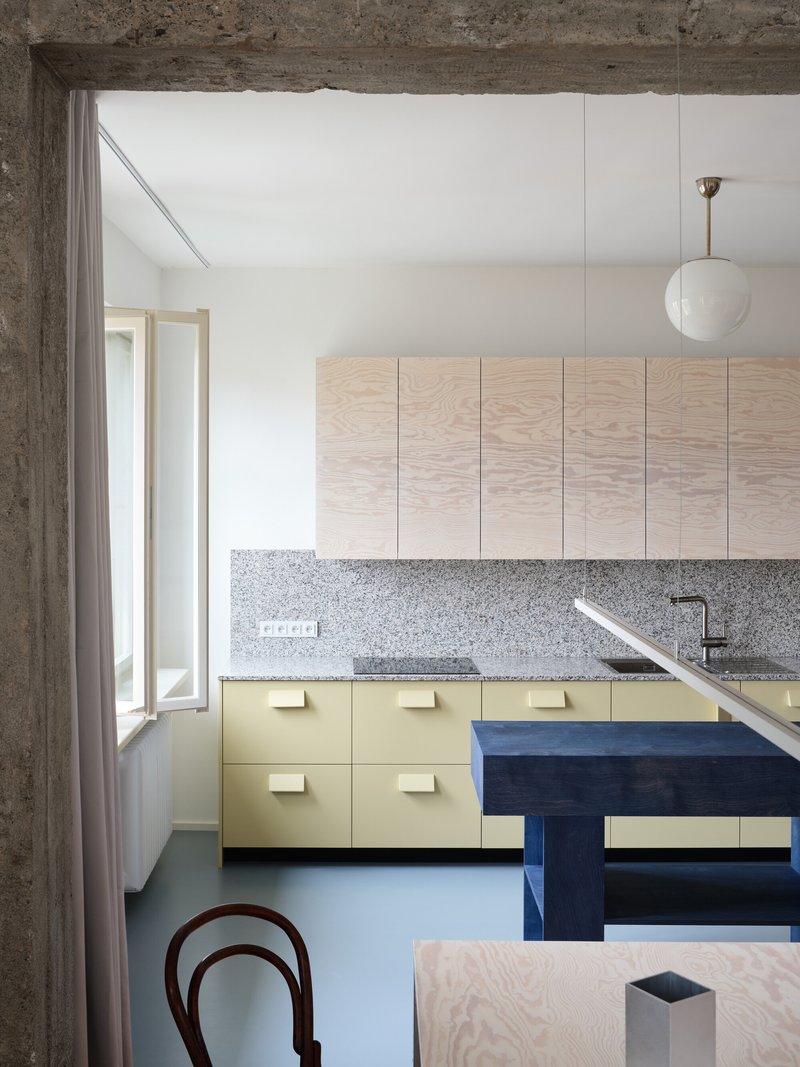 Kitchen view through concrete doorway with blue bench, yellow cabinets and hanging globe pendant