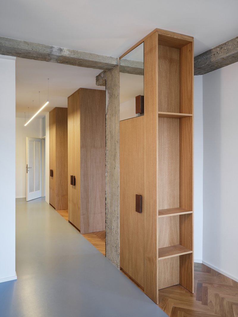 Hallway with tall oak cabinetry positioned between exposed concrete beams and grey resin flooring