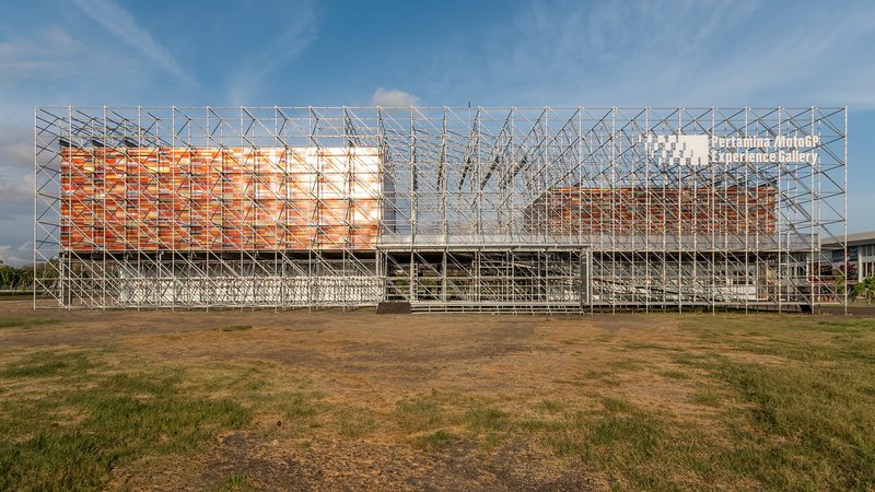 Exterior view of the tubular steel scaffolding structure enclosing orange woven panels across an open field
