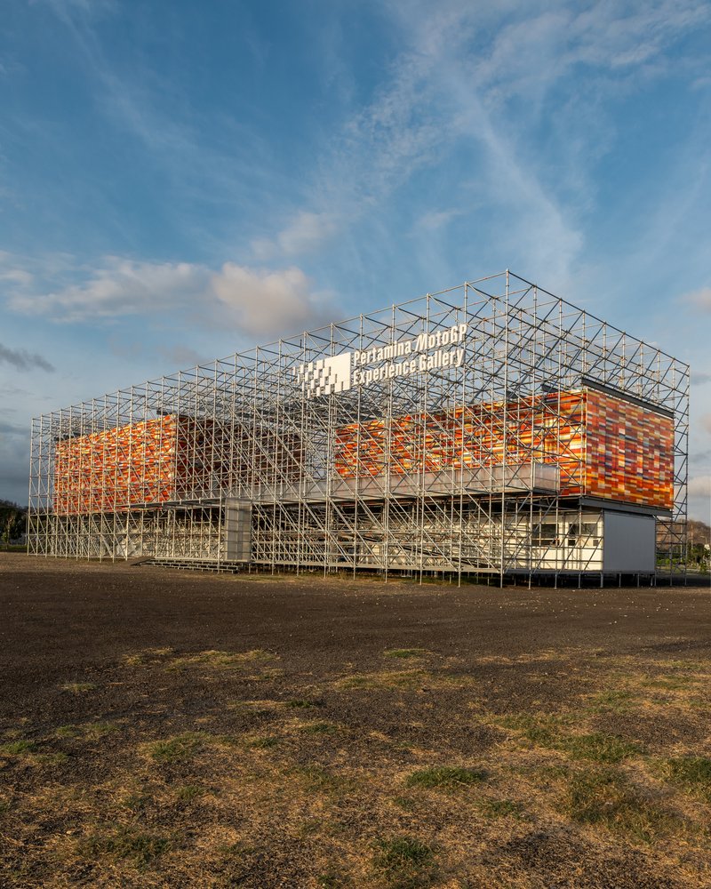 Corner perspective of the steel frame pavilion with woven orange facade under evening clouds