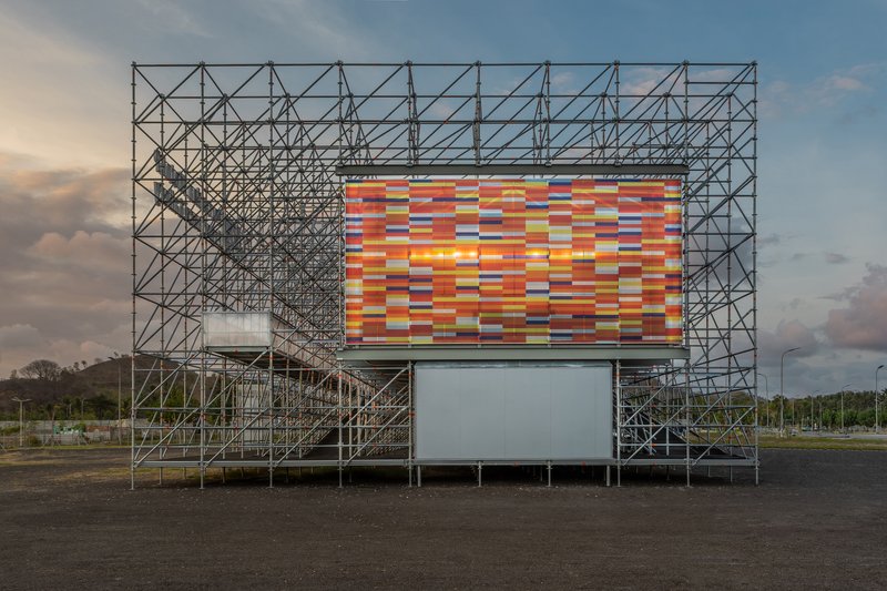 Tubular steel scaffolding structure with colorful striped panel facade at dusk under dramatic clouds