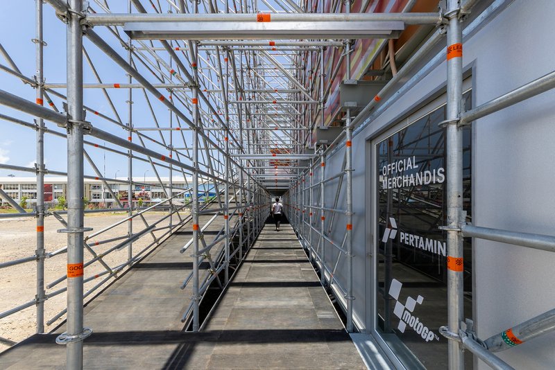 Narrow scaffolding walkway corridor with a visitor walking toward the colored panel wall