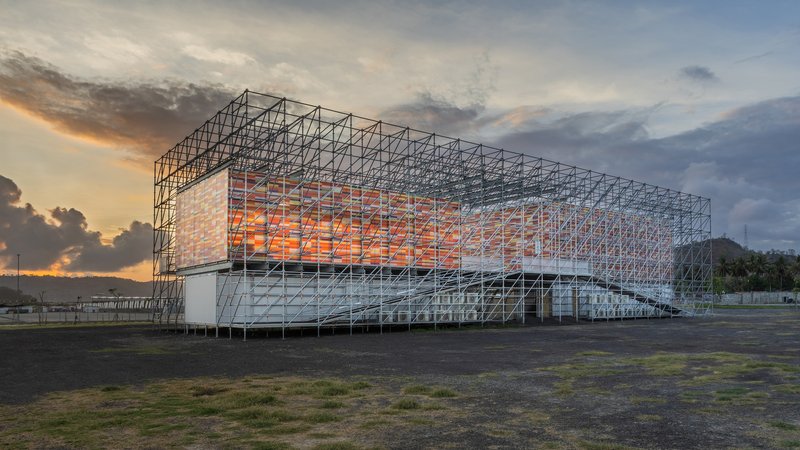 Steel frame pavilion with translucent orange panels glowing at dusk beneath dramatic storm clouds