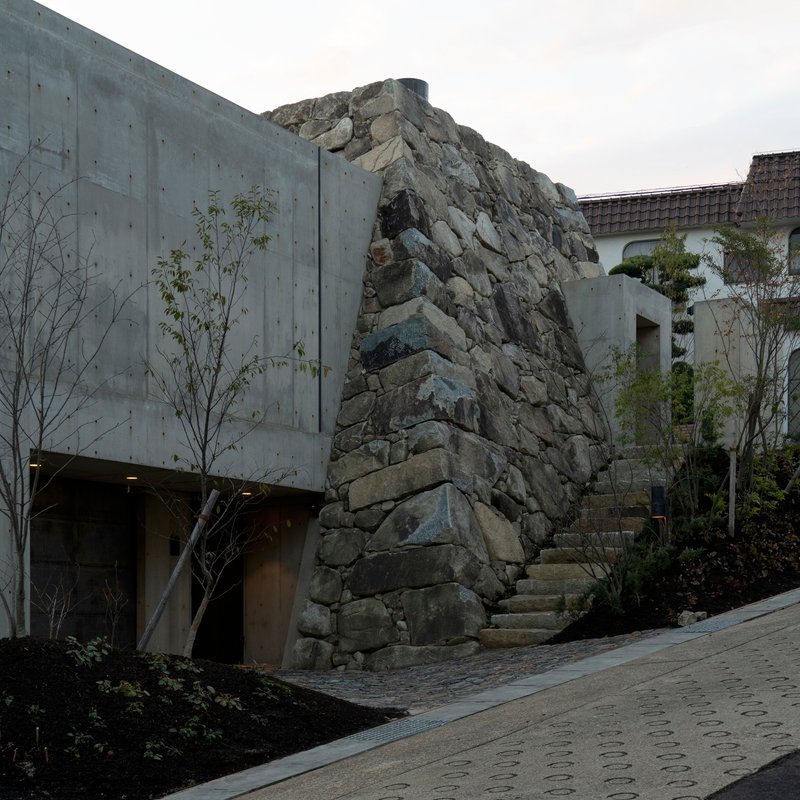 Exposed stone outcrop integrated into a concrete facade with planted beds and young trees below