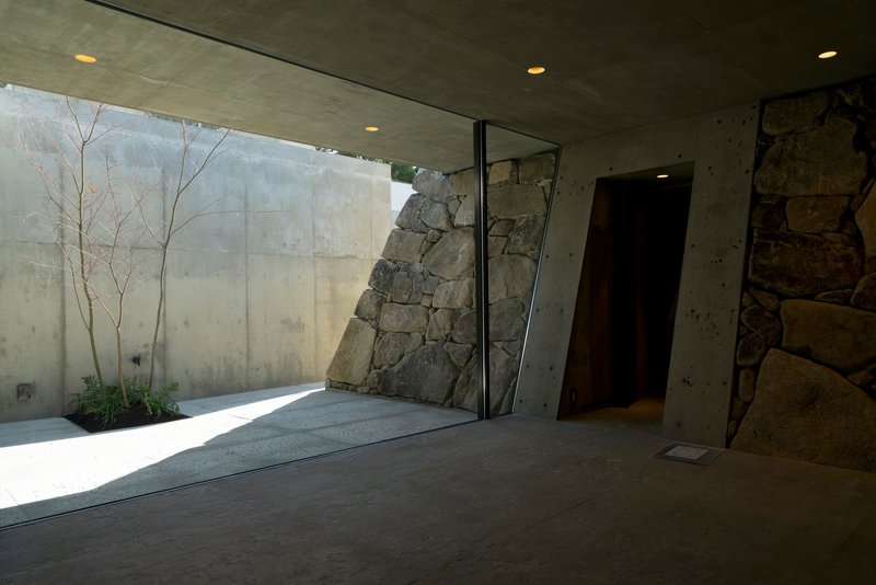 Corner view of the glass-walled courtyard showing the angled stone mass and planted bed