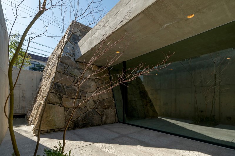 Courtyard terrace with bare tree branches against stone walls and a concrete canopy overhead