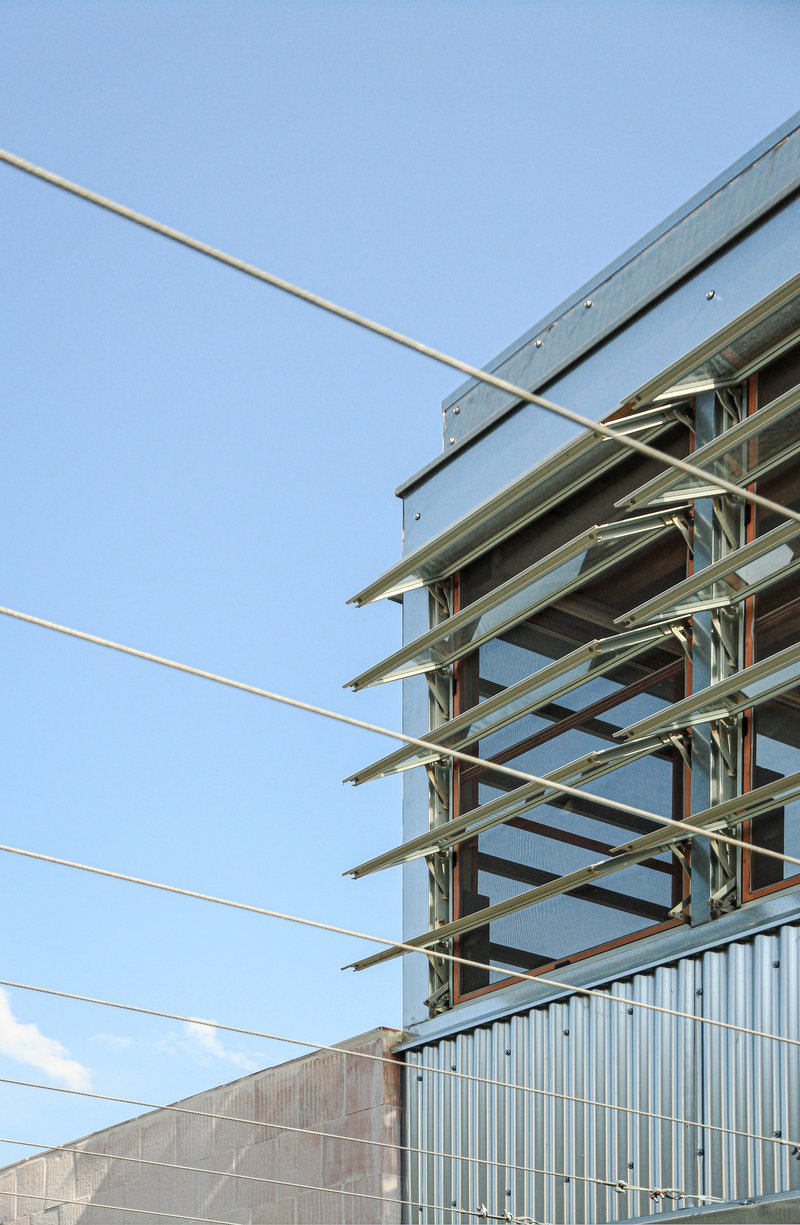 Exposed steel frame structure with horizontal beams crossing diagonal tension cables against a clear sky
