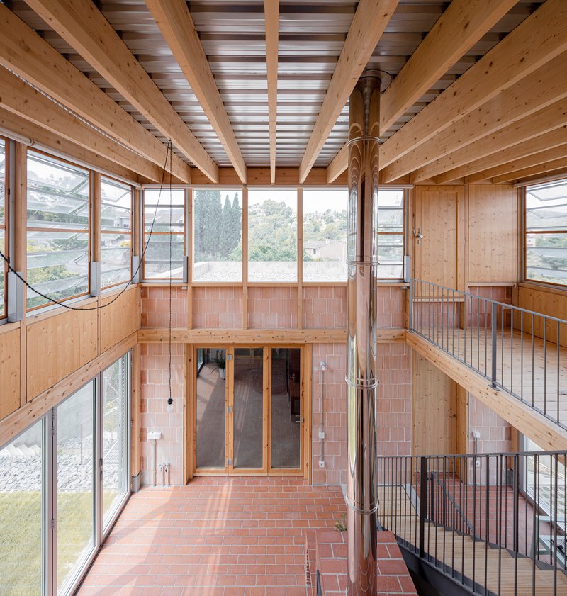 Upper-level interior view showing timber joists, clerestory windows, and steel railings overlooking the central brick floor