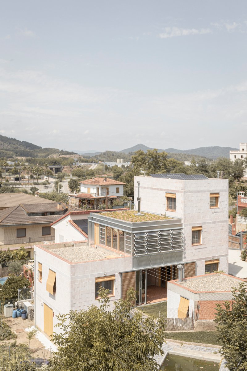 Elevated view of stacked masonry volumes with green roofs and timber louvres against distant hills
