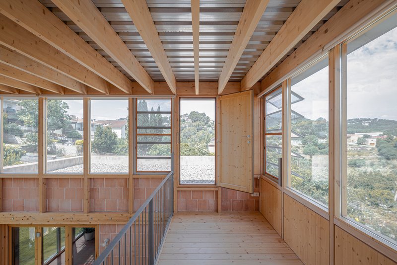 Interior timber-framed upper level with exposed joists, corrugated metal ceiling, and full-height glazing overlooking hills