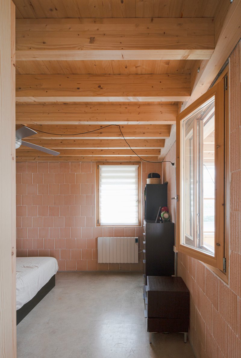 Bedroom with exposed timber beams, terracotta tile wall panels, and polished concrete floor