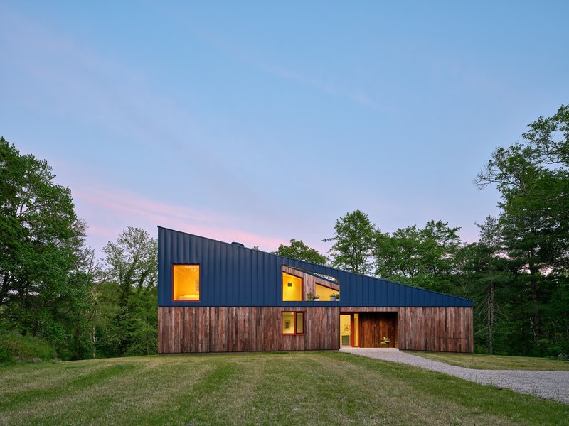 Timber and blue metal facade with illuminated windows at dusk against a pink sky