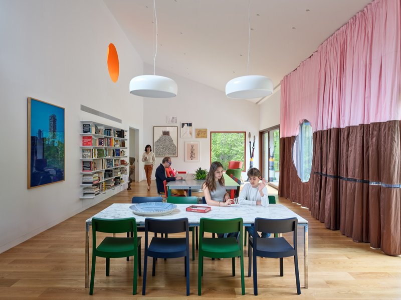 Open-plan living space with white dining table, pink and brown fabric partition, and family gathered throughout