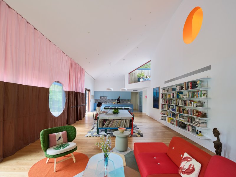 Living area with pink fabric divider, circular openings, oak flooring, and built-in bookshelves under vaulted ceiling