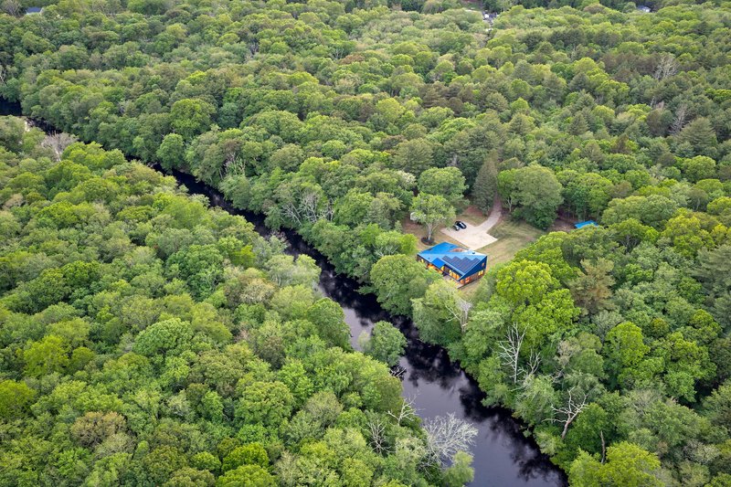 Drone view of the blue metal structure nestled at the edge of a creek in dense forest canopy