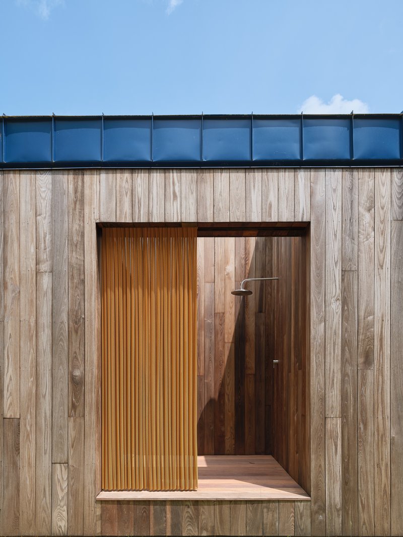 Timber-clad facade with inset vertical slat entry door and blue standing-seam metal roof above