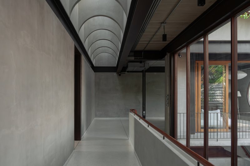 Upper corridor with vaulted concrete ceiling and timber-framed glazing overlooking an internal courtyard