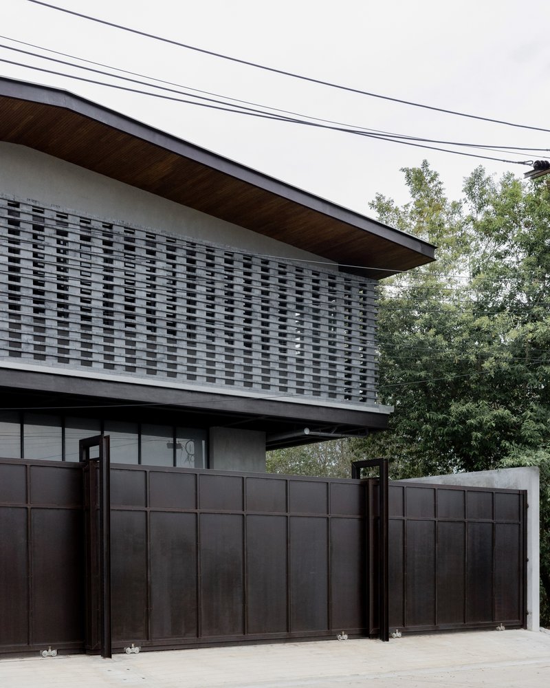 Detail of the woven brick screen wall above the metal gate with trees in the background