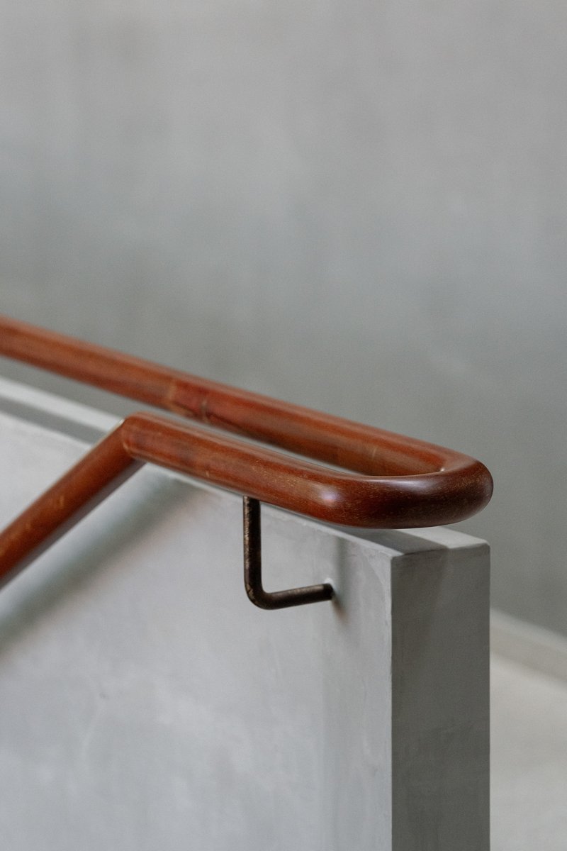Timber handrail with curved profile secured to concrete wall by black steel bracket
