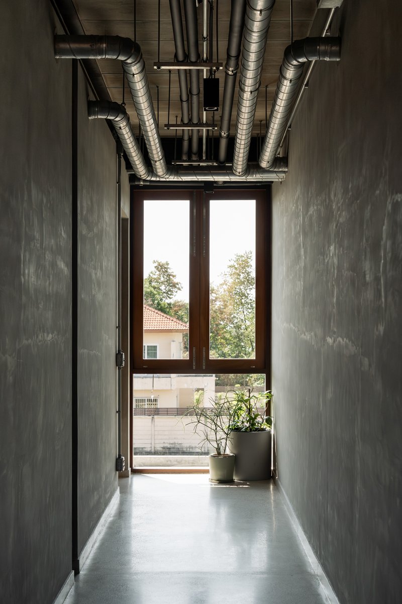 Concrete corridor with exposed ductwork overhead leading to glazed doors and potted plants