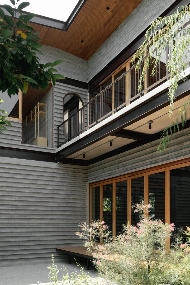 Courtyard view of stacked balconies with timber soffits, horizontal siding and planted beds below overhanging foliage