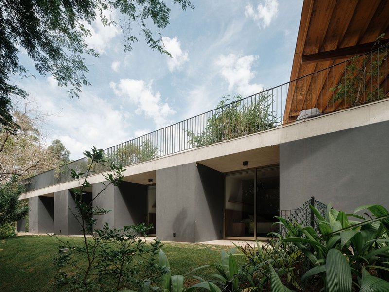 Concrete lower level facade with planted roof terrace balcony and steel railing under scattered clouds