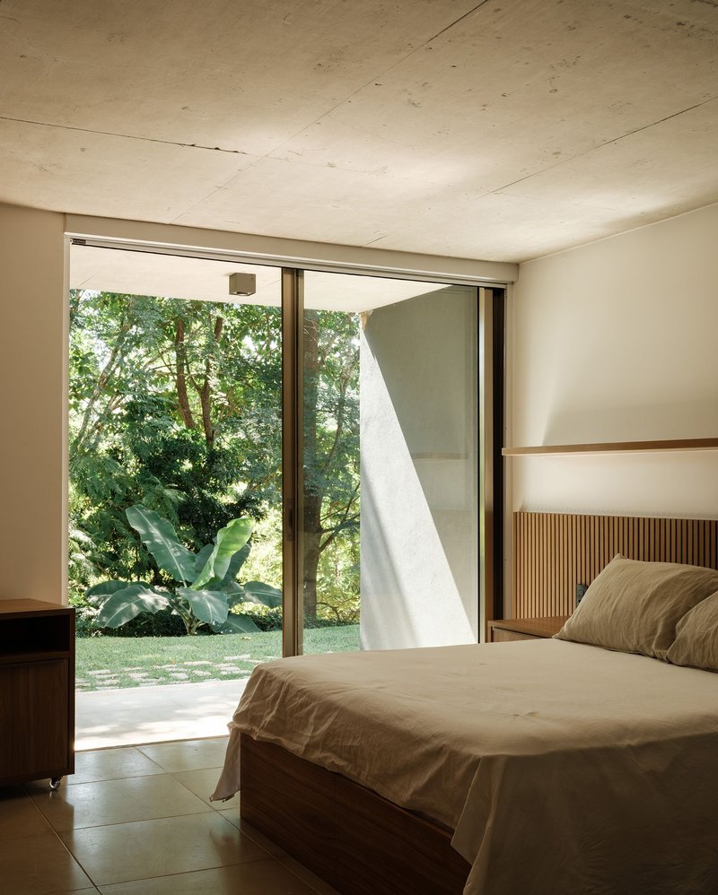 Bedroom with exposed concrete ceiling and sliding glass doors opening to garden with tropical plants