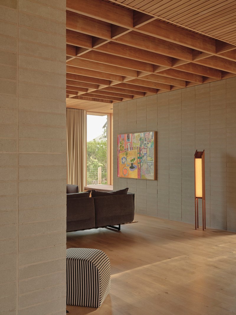 Interior living space with exposed timber beam ceiling and textured block wall opening to trees
