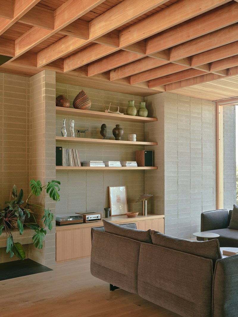 Built-in timber shelving with exposed beam ceiling and textured masonry wall beside a potted plant