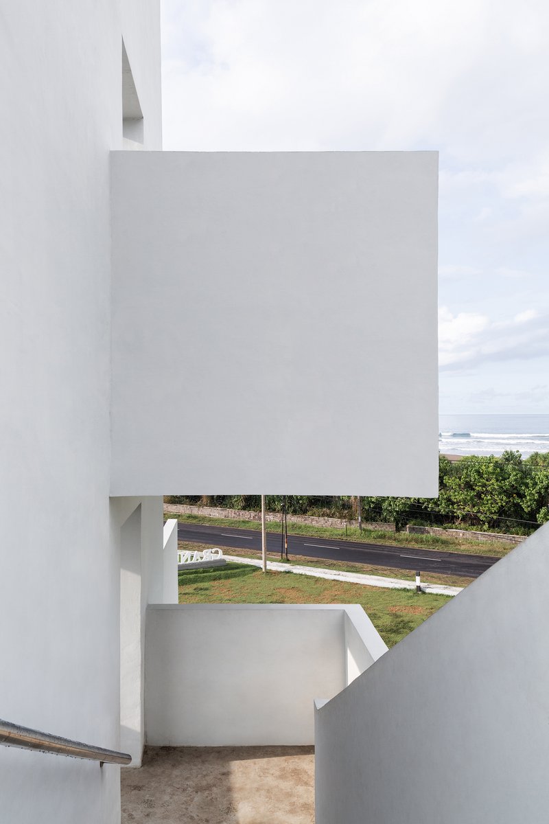 View through white-walled stairwell opening showing distant ocean and roadway beyond palm trees