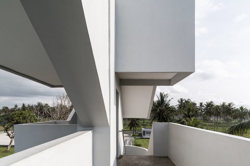 Upper-level outdoor passage with cantilevered slabs framing view of coconut palms and landscape