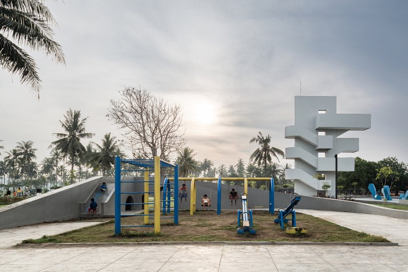Children playing on blue and yellow playground equipment beside the white concrete tower at dusk