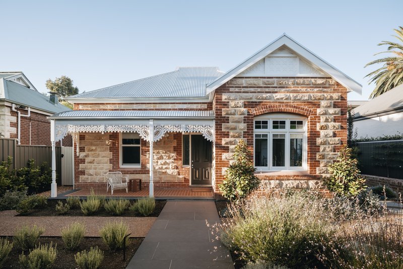 Street facade showing mixed red brick and sandstone walls with planted garden beds and palm tree