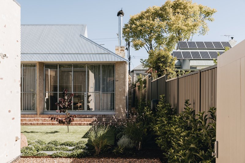Garden view showing corrugated metal cladding, stone walls and solar panels visible beyond planted beds
