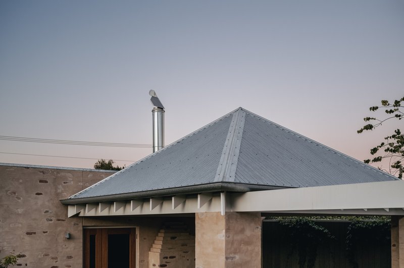 Hipped corrugated metal roof with chimney flue against a pale evening sky